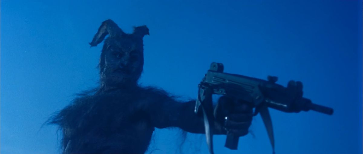 Una criatura demoníaca con cuernos que sostiene un subfusil MAC-10 contra un cielo azul.