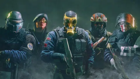 Foto promocional de Ubisoft Rainbow Six Siege, 5 soldados de diferentes ejércitos frente a la cámara. El Reino Unido está al frente y al centro con una máscara de gas amarilla y portando una escopeta. 