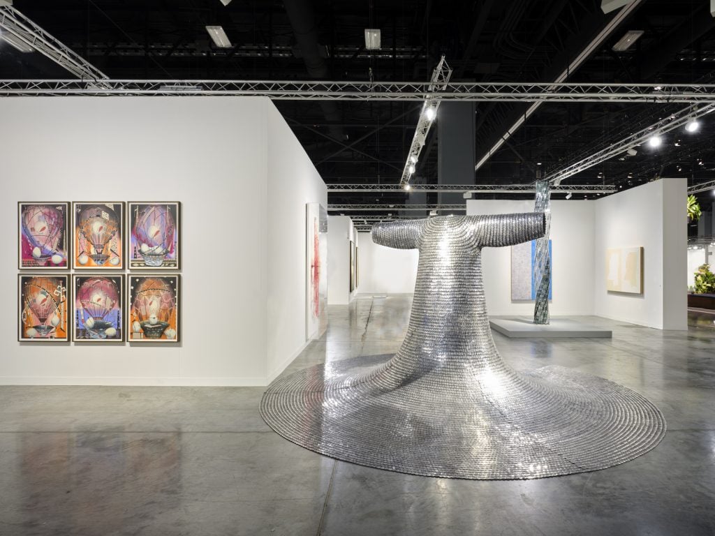 Un stand de paredes blancas con una gran escultura de metal y arte abstracto colorido en la pared.
