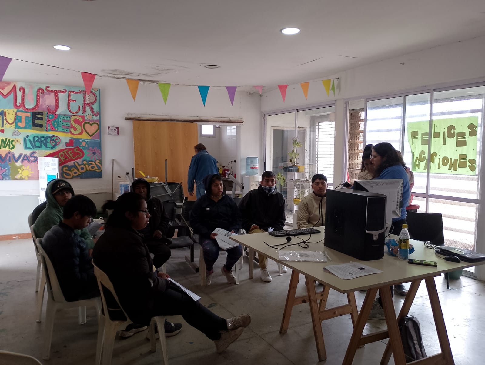 Grupo de personas alrededor de una mesa con una computadora en una habitación decorada con coloridos carteles y banderas
