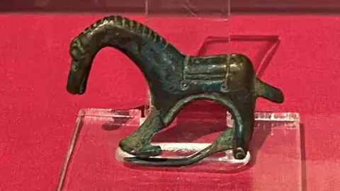 Policía de Lincolnshire Una figura de caballo de aleación de cobre con un cuello largo y curvo se encuentra sobre un soporte de luz sobre una mesa roja.